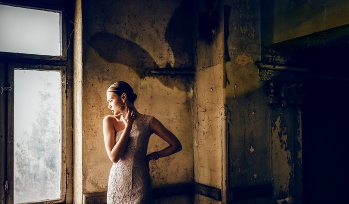 Woman in a dress by a window in a derelict room