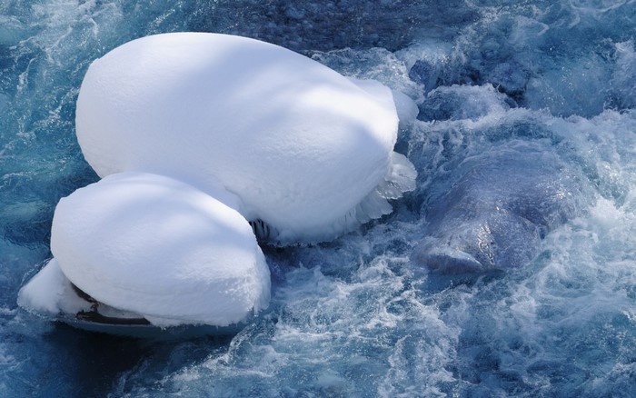 Snow-covered rocks in a rushing blue river