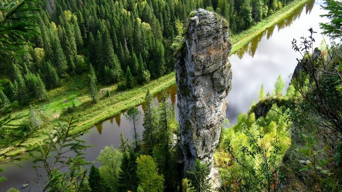 Tall Rock Formation Beside a Winding River in Forest
