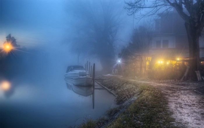 Boat docked by a misty house with lights on