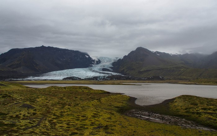 Glacier and lake in a mountainous landscape under cloudy sky