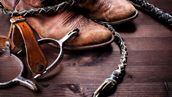 Cowboy boots, spurs, and whip on wooden surface