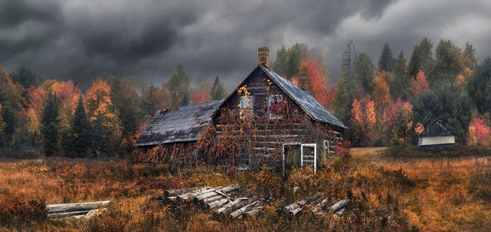 Abandoned cabin in autumn forest under stormy clouds