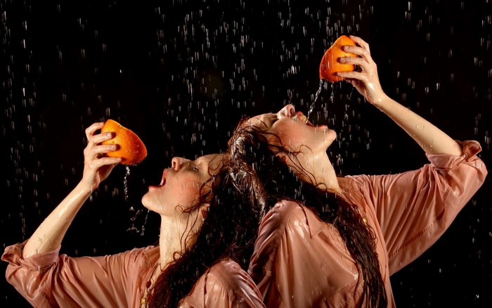 Two women in wet shirts squeezing oranges