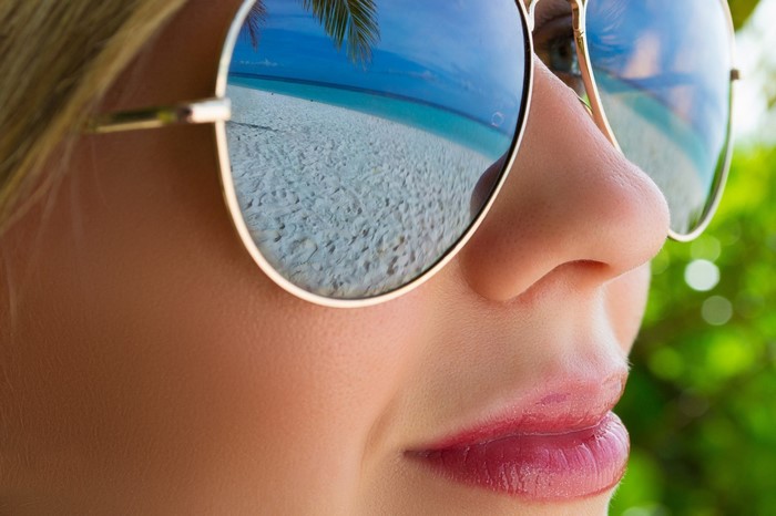 Close up of a woman wearing sunglasses reflecting a beach