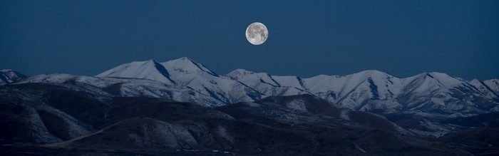 Full moon over snow-capped mountains at night