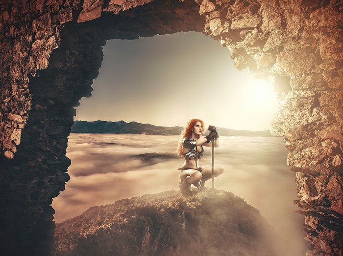 Fantasy warrior woman with sword in rocky archway over clouds