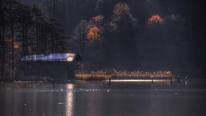 Cabin by a misty lake in autumn with sun rays