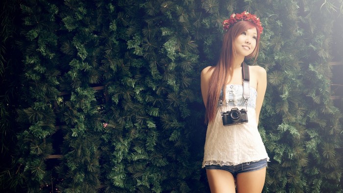 Woman with flower crown and camera in front of greenery