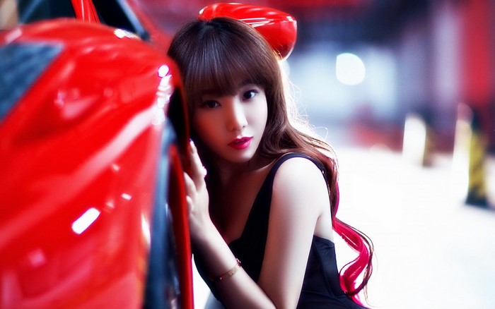 Asian woman in black dress leaning on red car