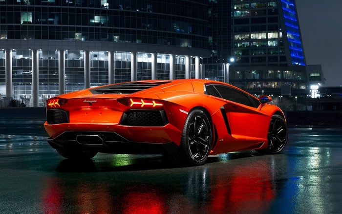 Orange Lamborghini Aventador parked on wet city street at night