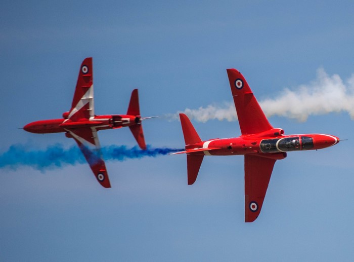 Two red airplanes performing aerobatics with smoke trails
