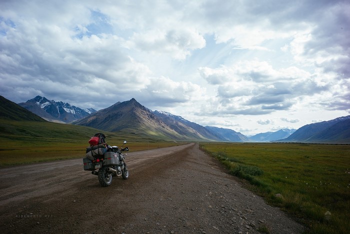 Motorcycle on a dirt road with mountains and clouds