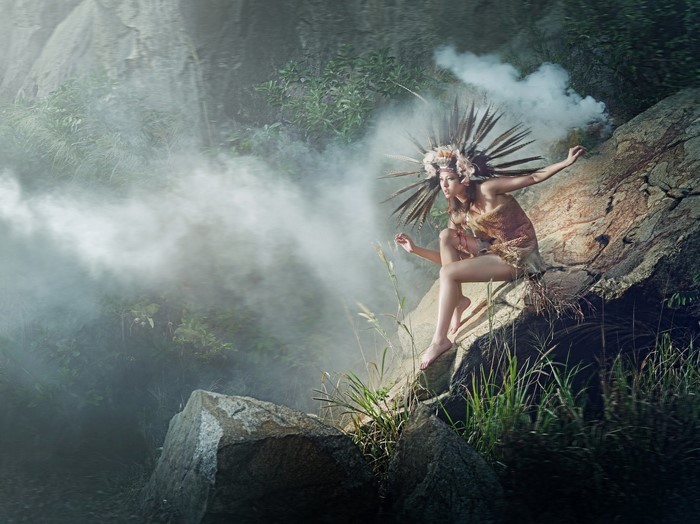 Woman in headdress sitting on a rock in a misty forest