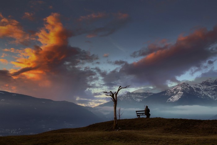 Person on bench watching sunset over mountains