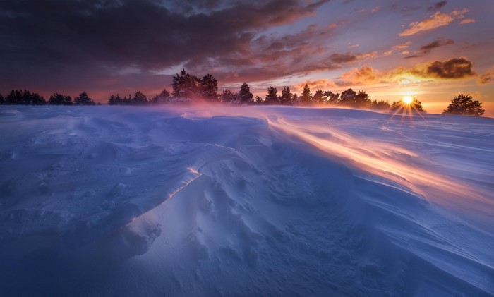 Snowy landscape at sunset with wind blowing snow