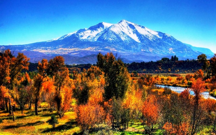 Snowy mountain range over autumn trees and river