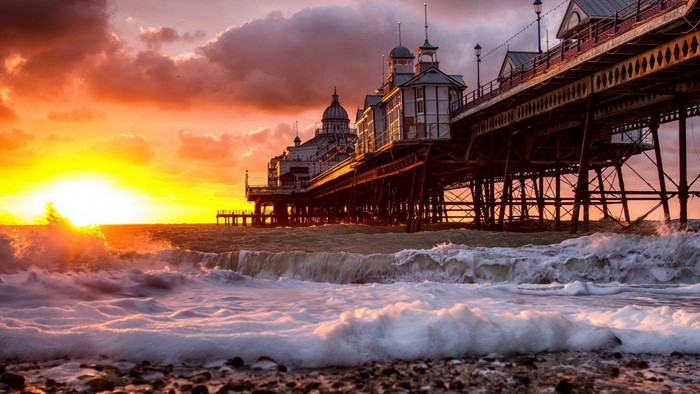 Sunset over a pier with waves crashing on the shore