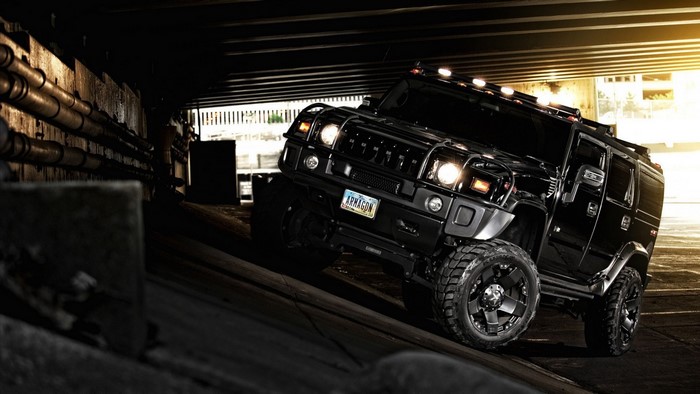 Black Hummer H2 SUV driving under a bridge