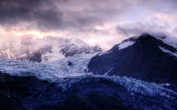 Glacier and snow-capped mountains under cloudy sky
