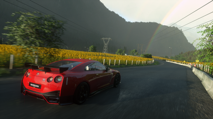 Red Nissan GT-R driving on a road with sunflowers and mountains