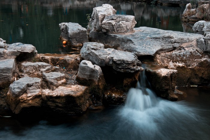 Long exposure of a small waterfall cascading over rocks into a dark body of water