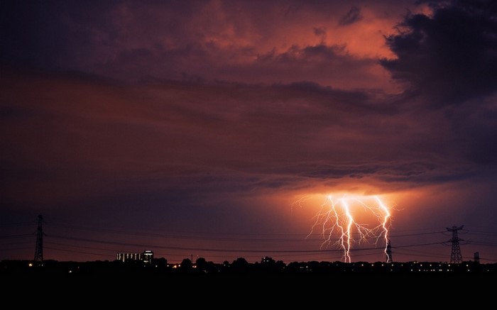 Lightning strikes over a silhouetted cityscape at dusk