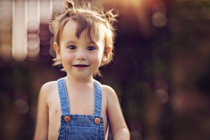Toddler girl in denim overalls smiling outdoors