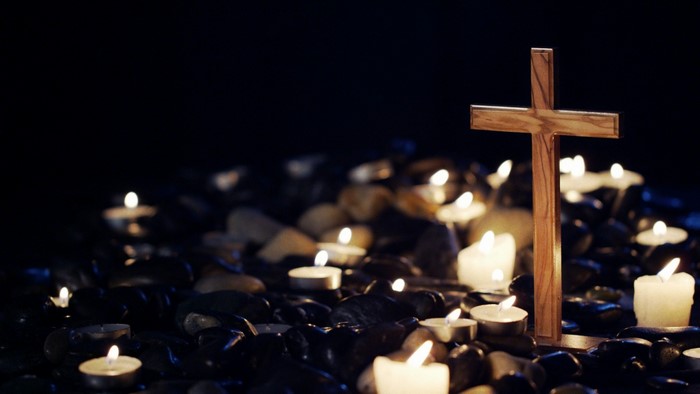 Wooden cross surrounded by lit candles in darkness