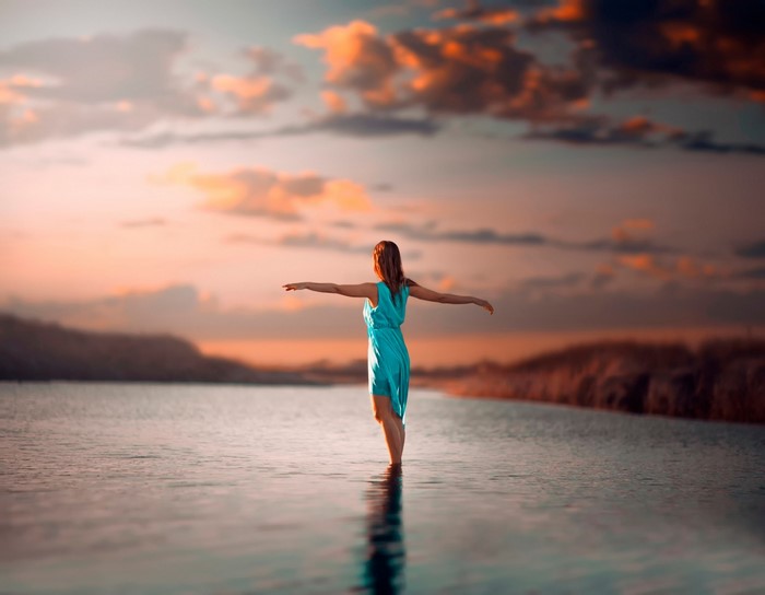 Woman in blue dress standing in water at sunset