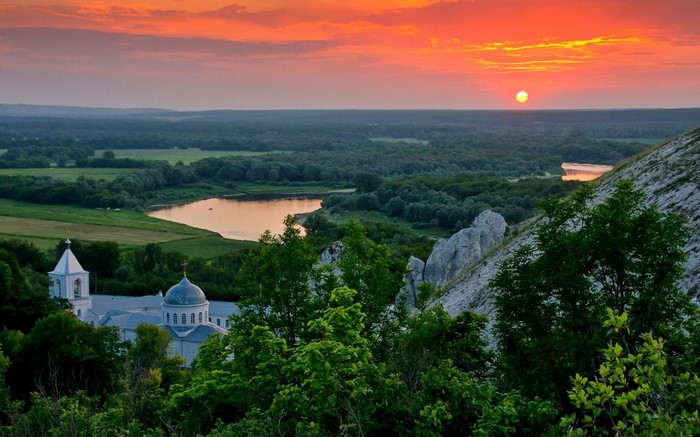 Monastery on a hill overlooking a river at sunset