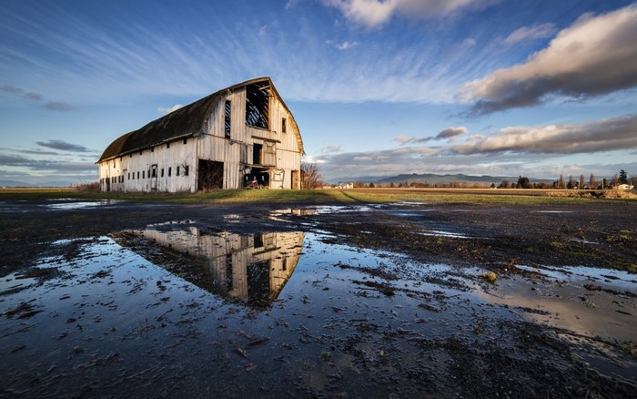 Old barn reflected in a puddle under a cloudy sky