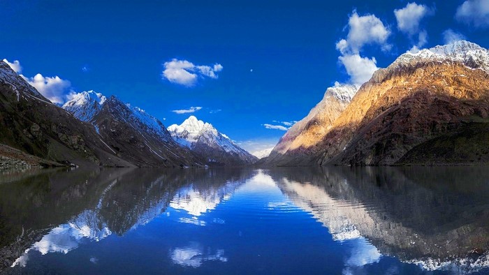 Snowy mountains reflected in a lake under a blue sky