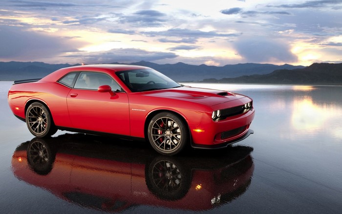 Red Dodge Challenger parked on wet surface with mountains