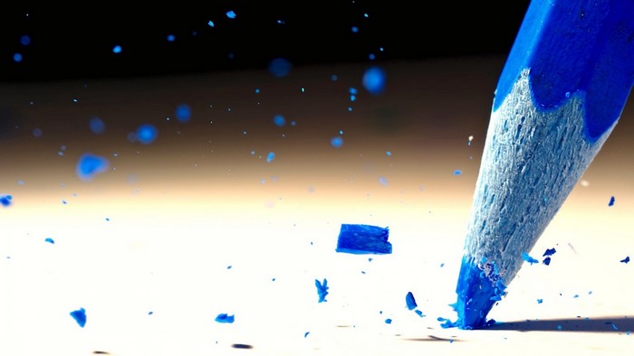 Blue pencil breaking on a white surface with blue fragments flying