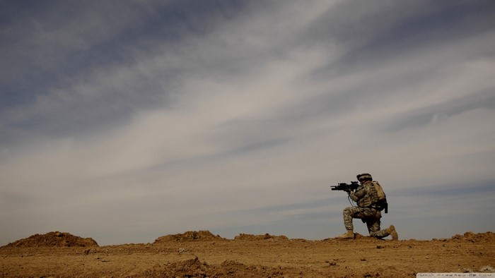 Soldier kneeling with rifle in desert landscape