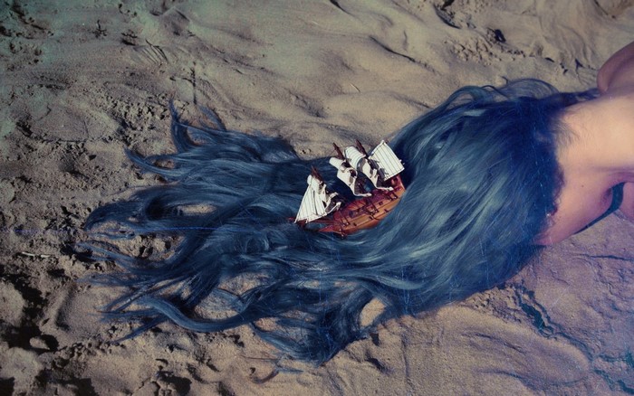 Model with blue hair and a ship on sand