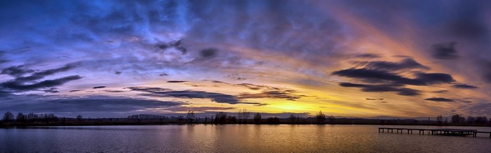 Panoramic sunset over a lake with a pier