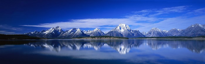 Snow-capped mountains reflected in a calm lake under a blue sky