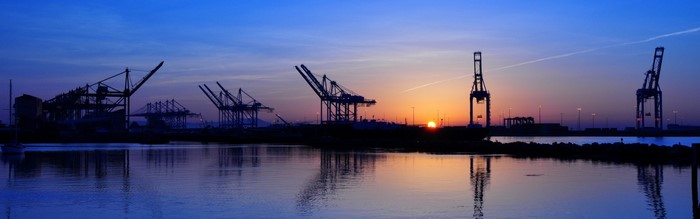 Port cranes at sunset over water with reflections