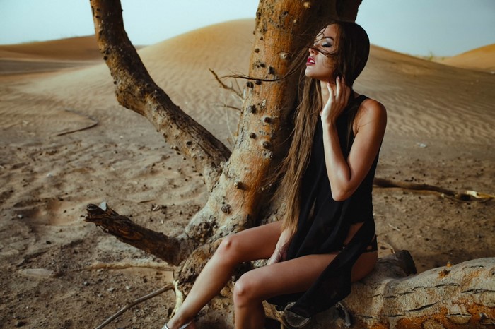 Woman in black clothing sitting by a tree in the desert