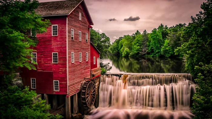 Red mill building with a water wheel next to a waterfall