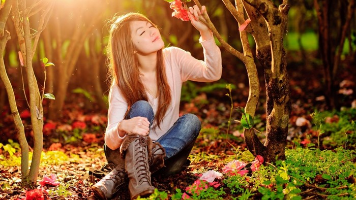 Young woman smelling a flower in a sunlit forest