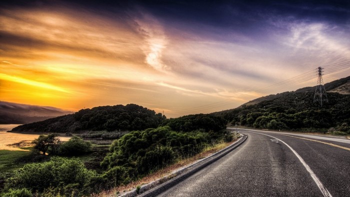 Road winding through hills at sunset with power lines