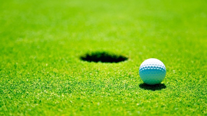 Golf ball on a green golf course near a hole
