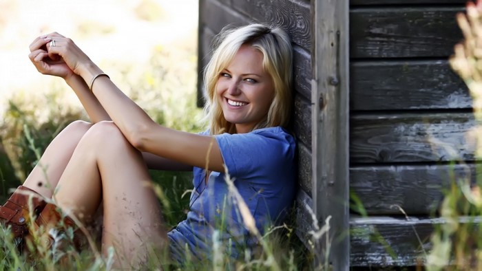 Malin Akerman sitting in grass by a wooden structure