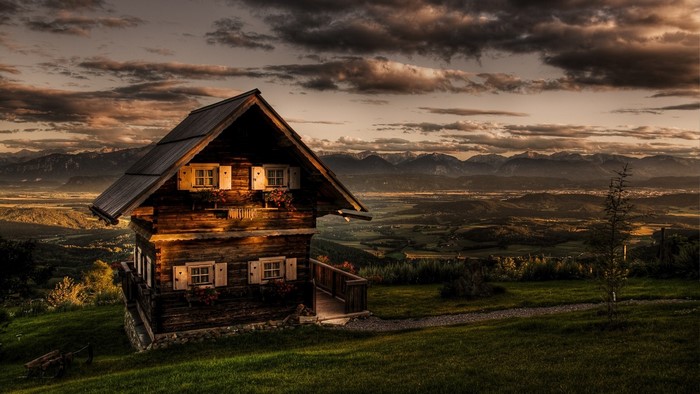 Wooden cabin on a hill overlooking mountains at sunset