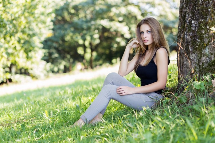 Woman with blue eyes sitting in grass near a tree