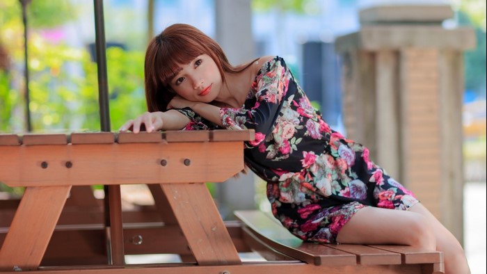 Woman in Floral Minidress Sitting Outdoors on Wooden Bench