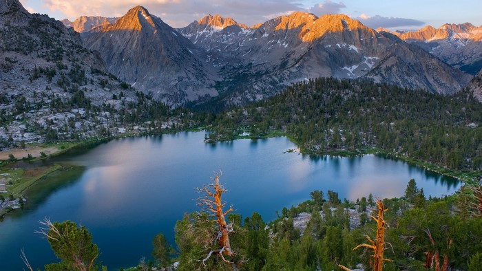 Mountain lake with trees and rocky peaks at sunset